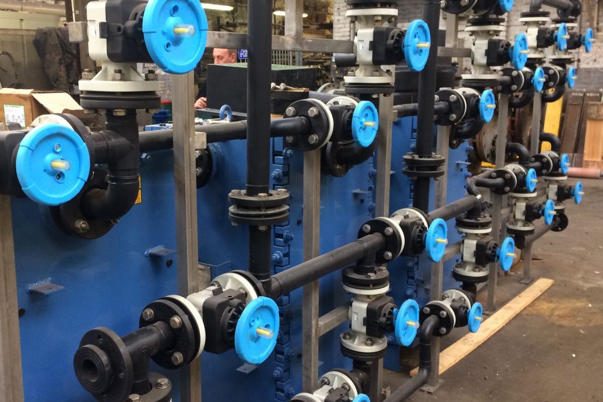 Rows of thermoplastic valves with blue handwheels on dark plastic pipework, mounted on panel skids in a workshop.